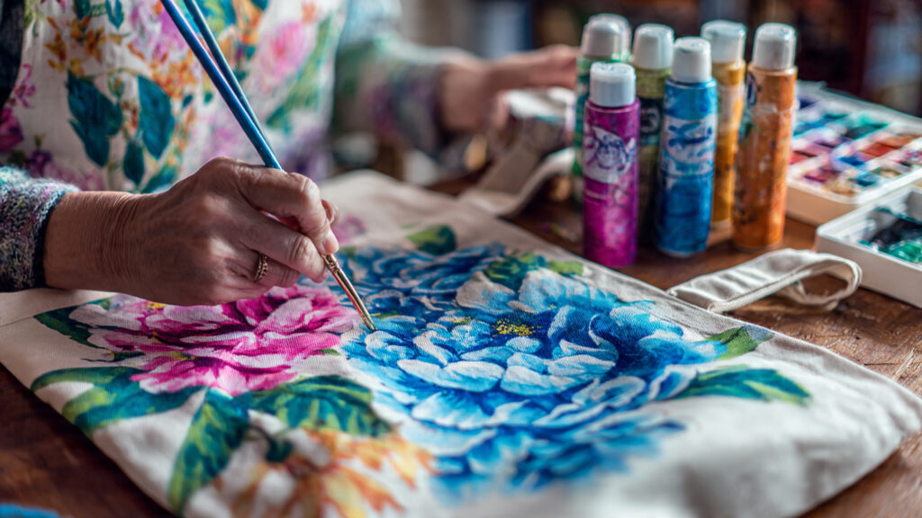 Creative Craft Ideas to Try at Home in 2026 artist painting floral design on fabric tote bag w